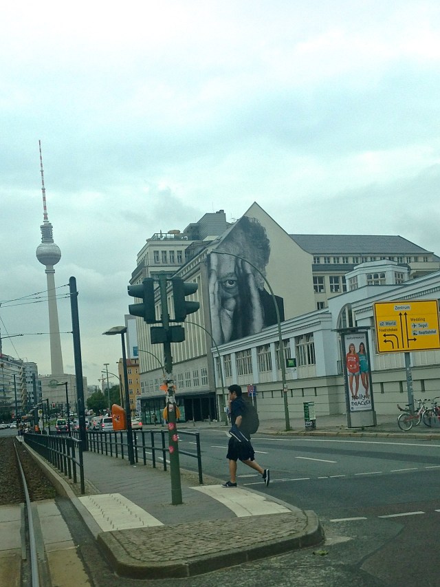 A street art work by French artist, JR, peeks out against a background of the Fernsehturm, the Berlin TV tower