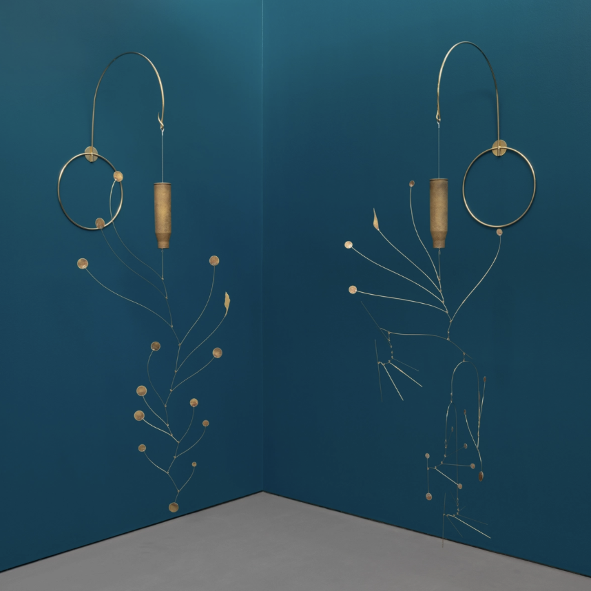 Two metallic wall sculptures with abstract floral designs, featuring circular and elongated shapes, mounted on a deep blue wall.