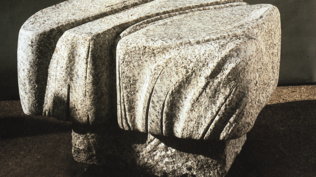 A sculptural stone table with a textured surface and organic, flowing shapes, set against a dark background.